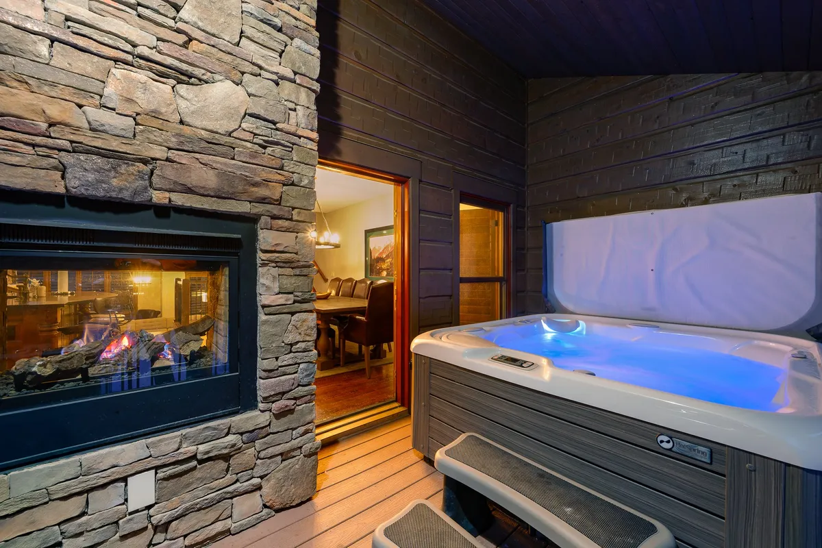 An exterior view of a private hot tub and fireplace adjacent to a dining area, suggesting a serene après-ski environment ideal for unwinding and socializing after active days on the mountain.