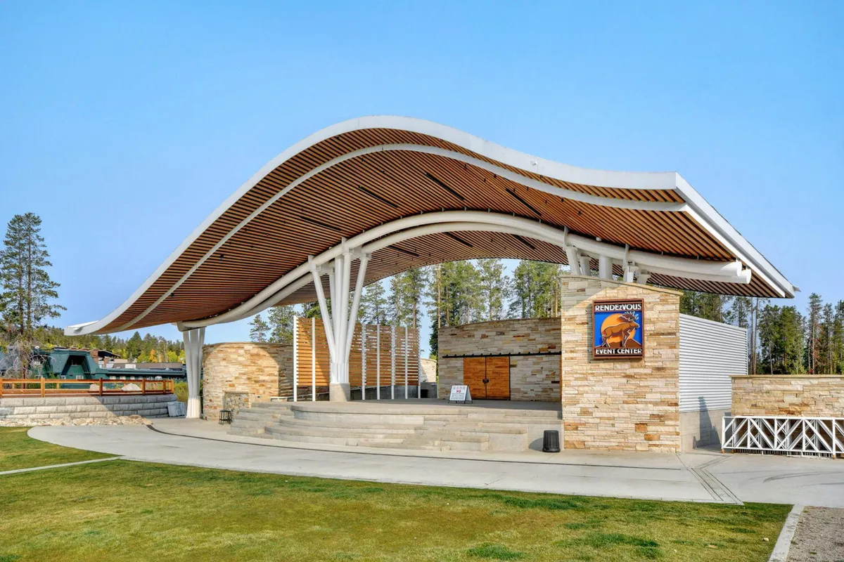 This image features the iconic curved roof structure and stone facade of an outdoor amphitheater, with a stage area ready for performances. The setting suggests a lively community atmosphere, ideal for concerts, festivals, and public gatherings under the open sky.