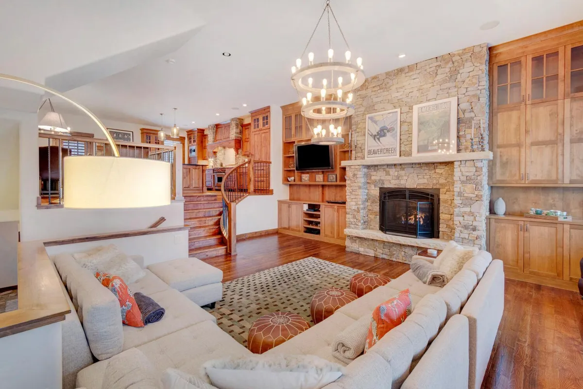 A warm, inviting living room scene featuring a glowing fireplace, plush sofa, and elegant chandelier. The space exudes a cozy ambiance, ideal for fireside gatherings after a day of winter activities. Large windows hint at the outdoor scenery and allow natural light to fill the room.