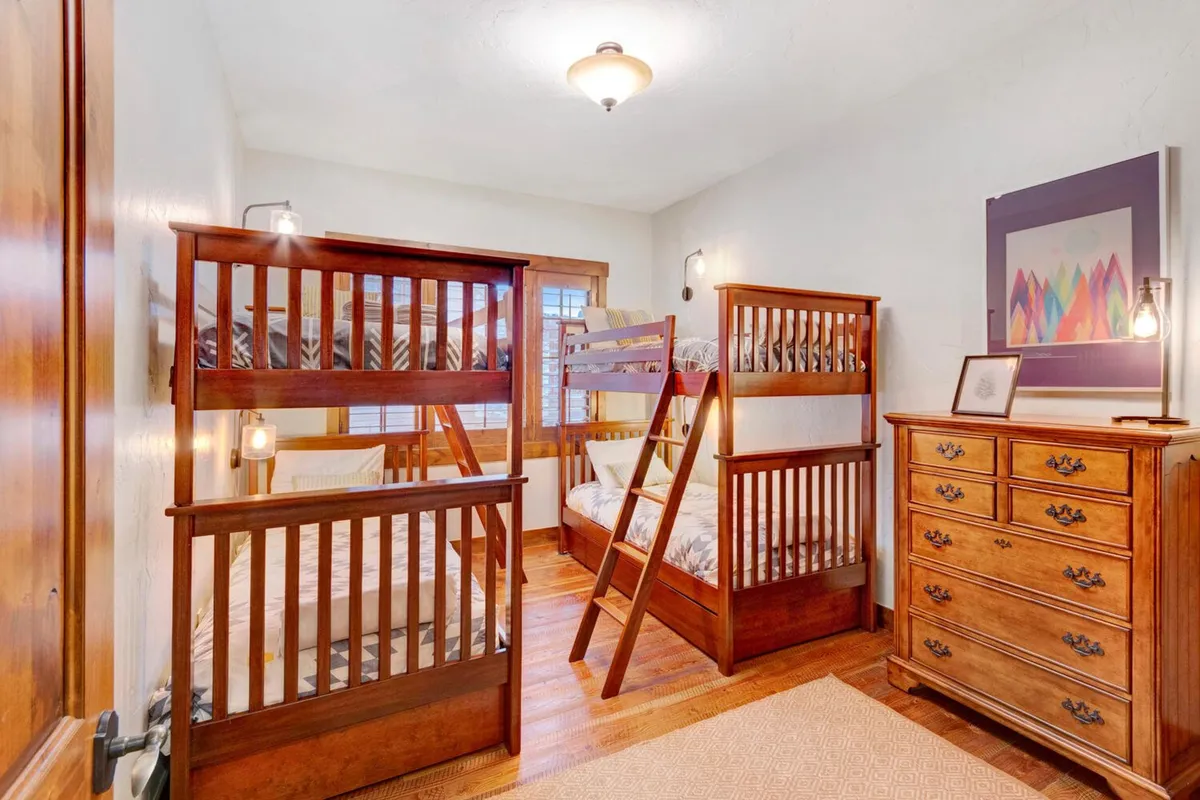 A cheerful bunk room featuring sturdy wooden bunk beds with colorful linens, a playful dresser, and bright artwork. The space feels inviting for children or groups, with an energetic yet cozy mood ideal for bedtime stories or sleepovers.