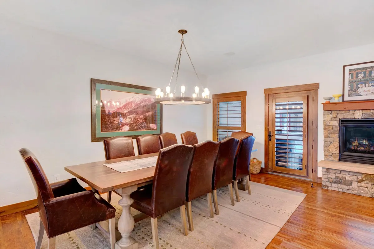 An elegant dining space with a large wooden dining table set beneath a glowing chandelier. The table is surrounded by ample seating, complemented by a fireplace in the background and stylish wall art. The space feels both intimate and perfect for group gatherings or celebratory meals.